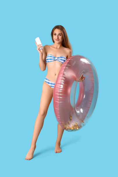 Young woman with sunscreen cream and inflatable ring on blue background - Fotó, kép