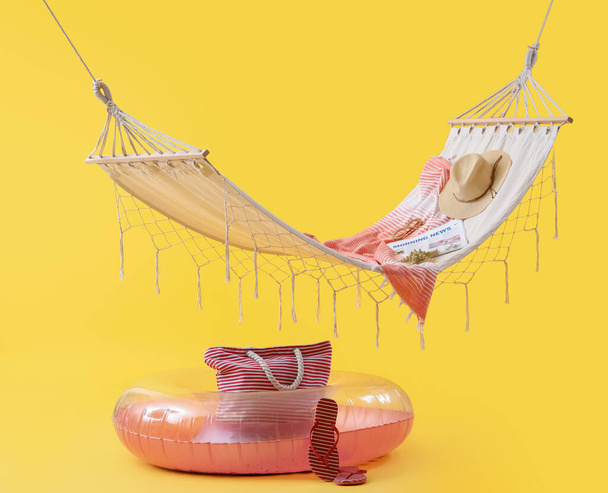 Przytulny hamak z nadmuchiwanym pierścieniem i różnymi akcesoriami plażowymi na żółtym tle. Koncepcja wakacji letnich - Zdjęcie, obraz
