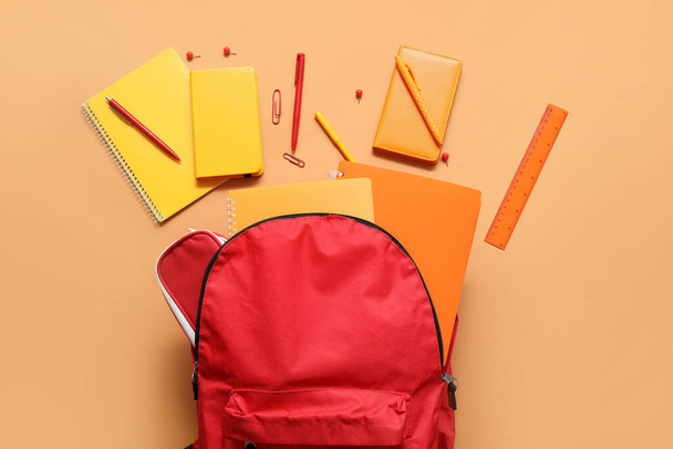 Roter Schulrucksack mit Notizbüchern, Stiften und Lineal auf orangefarbenem Hintergrund - Foto, Bild
