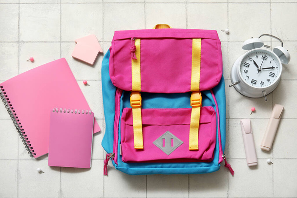 Цветной школьный рюкзак с ноутбуками, будильником и маркерами на белом фоне плитки - Фото, изображение