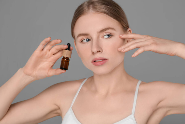 Beautiful young woman with bottle of essential oil on light grey background - Fotografie, Obrázek