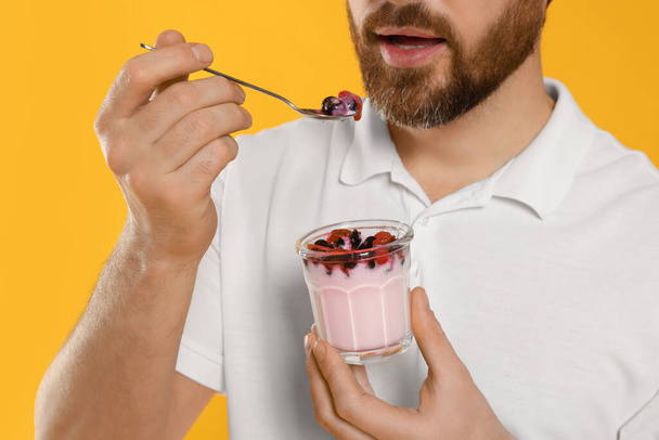 Man eating delicious yogurt on yellow background, closeup - Fotografie, Obrázek