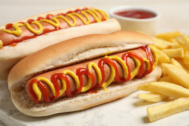 Delicious hot dogs with mustard, ketchup and potato fries on table, closeup - Foto, Bild