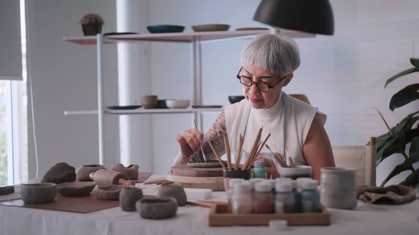 Evde çömlekçilik yapmaktan hoşlanan Asyalı yaşlı kadın. Bir kadın seramikçi stüdyoda yeni çömlekler yapıyor.. - Fotoğraf, Görsel