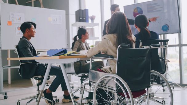A disabled company employee is able to work happily with colleagues in the office. A group of marketers are having a discussion at the meeting. - Фото, изображение
