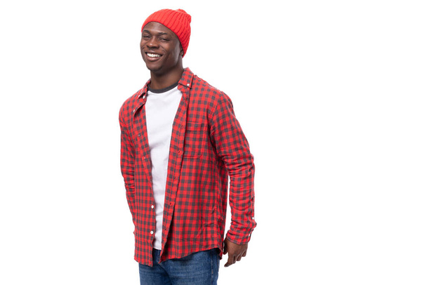 Porträt eines verträumten bescheidenen schwarzen amerikanischen Mannes der 30er Jahre in rotem Hemd und Mütze auf weißem Studiohintergrund mit Kopierraum. - Foto, Bild
