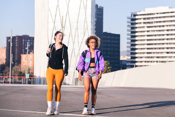 two friends walking along a city ready to run in a sunny day, concept of friendship and urban sport, copy space for text - Foto, Imagen