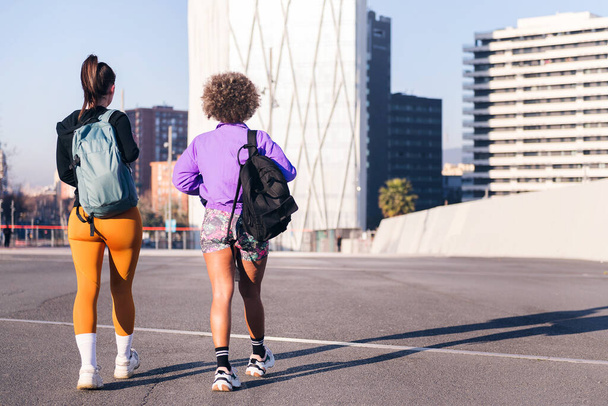 rear view of two unrecognizable friends walking along a city ready to run in a sunny day, concept of friendship and urban sport, copy space for text - Foto, Bild
