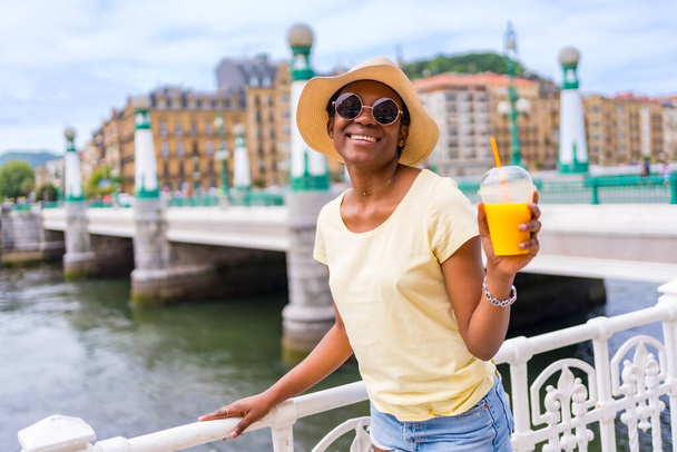 Portrait of black ethnic woman having an orange juice enjoying summer on vacation - 写真・画像