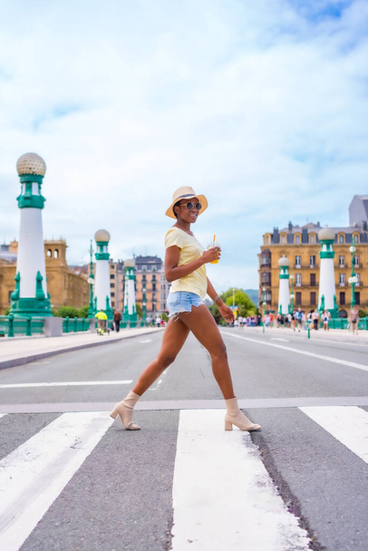 Portrait de femme noire ethnique ayant un jus d'orange profitant de l'été en vacances traversant la rue - Photo, image