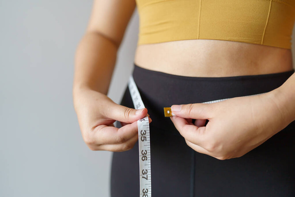 жінка хоче схуднути з сантиметром Формуйте здоровий м'яз шлунка і дієту вимірюючи талію з мірною стрічкою після контролю ваги дієти
. - Фото, зображення