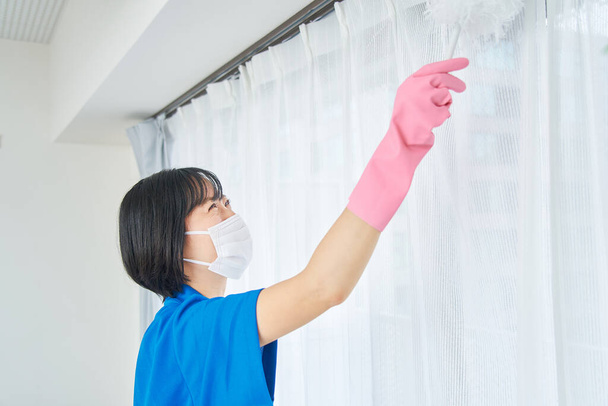 Μια γυναίκα με ρούχα εργασίας που καθαρίζει το δωμάτιο. - Φωτογραφία, εικόνα