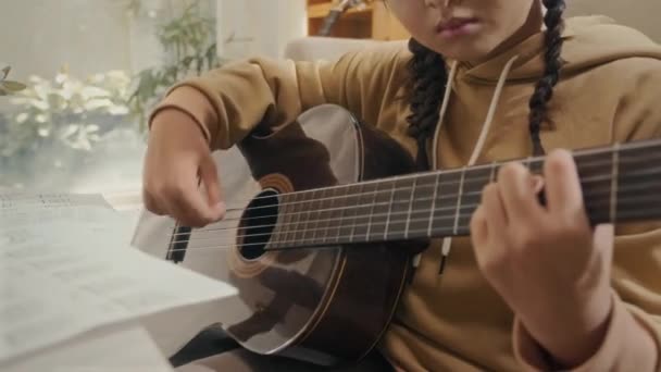 Teenage student dělat poznámky v copybooku, zatímco se učí hrát na kytaru sedí doma - Záběry, video