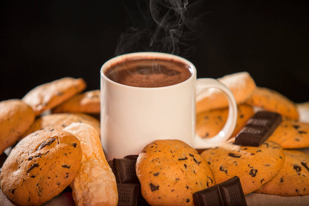 Tasse heiße Schokolade mit Keksen und Unzen Schokolade vor schwarzem Hintergrund - Foto, Bild