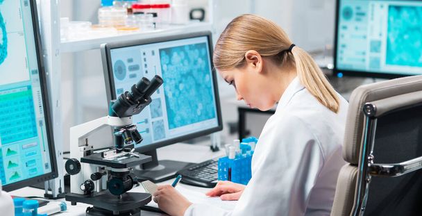 Professional female scientist is working on a vaccine in a modern scientific research laboratory. Laboratory tools: microscope, test tubes, equipment. Future technology, healthcare and science concept - Foto, imagen