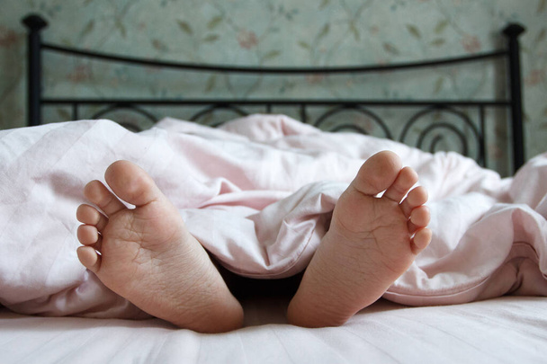 Feet under a light blanket on the bed. Concept of sleeping or waking in the morning - Fotoğraf, Görsel