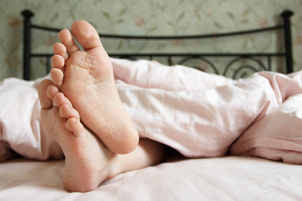 Feet under a light blanket on the bed. Concept of sleeping or waking in the morning - Foto, immagini