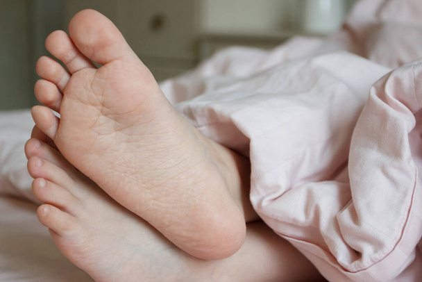 Feet under a light blanket on the bed. Concept of sleeping or waking in the morning - Foto, Imagem