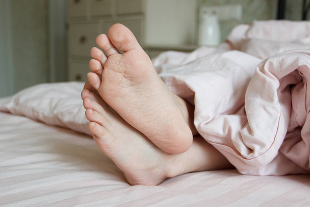 Feet under a light blanket on the bed. Concept of sleeping or waking in the morning - Φωτογραφία, εικόνα
