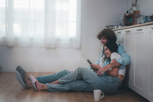 Una giovane coppia parla mentre è seduta sul pavimento della cucina. giovane coppia avendo un buon tempo insieme a casa. - Foto, immagini