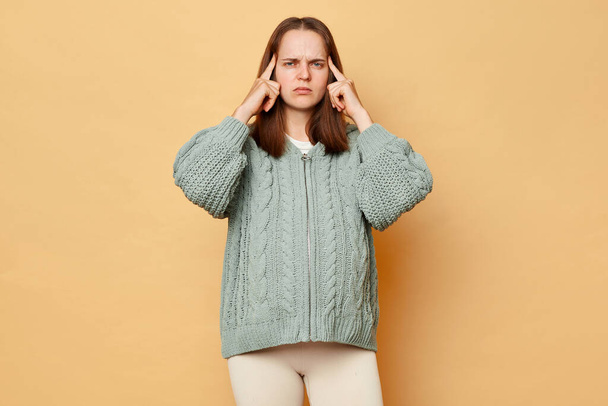 Unhealthy pregnant woman wearing warm knitted sweater touching painful temples posing over beige background suffering terrible headache during pregnancy. - Фото, изображение