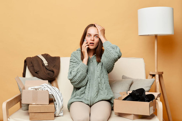 Shocked sad unhappy woman sitting on sofa opening carton box talking on mobile phone checking her order talking to assistant has problems with delivery. - Foto, Imagem