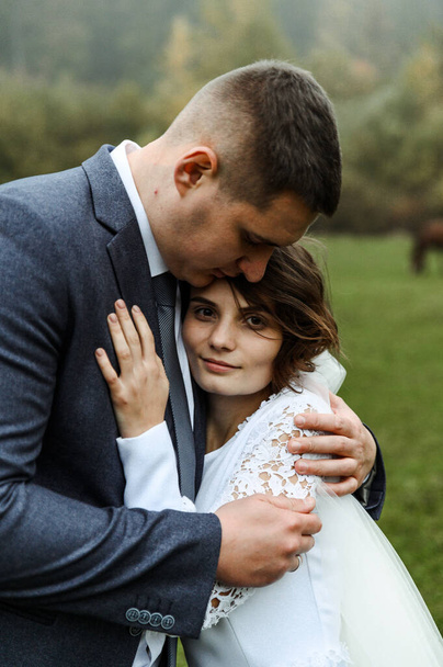 young wedding couple outdoors in the autumn season. autumn wedding day. height difference. the groom hugs the bride to him. the newlywed on the background of fog and fallen leaves - Foto, afbeelding