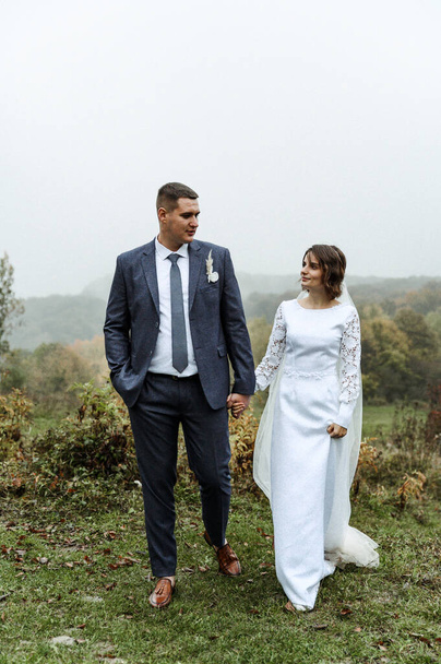 young wedding couple outdoors in the autumn season. autumn wedding day. height difference. the groom hugs the bride to him. the newlywed on the background of fog and fallen leaves - Φωτογραφία, εικόνα