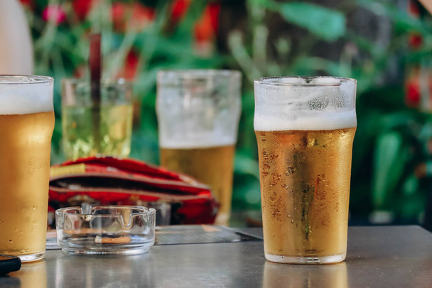 Cztery zimne kieliszki z piwem na stole i przyjaciele rozmawiający przy szklance - Zdjęcie, obraz