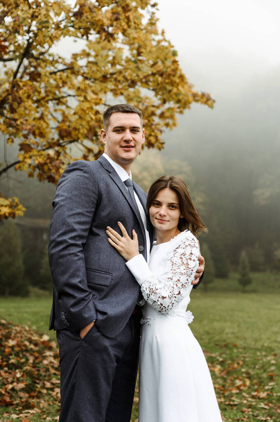 tall bride and groom hugging against the backdrop of autumn nature. walk of a cute couple in nature. newlyweds after the ceremony. wedding day in autumn - Zdjęcie, obraz