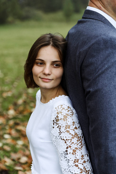 wedding walk in the autumn park. newlyweds with a difference in height. wedding couple after the ceremony. couple holding hands tightly. - Фото, зображення