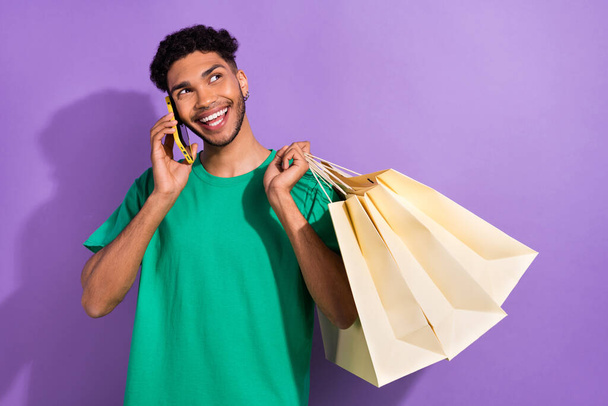 Photo of handsome guy speak communicate telephone hold boutique bags isolated on violet color background. - 写真・画像