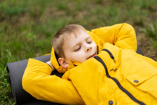 A young boy in a jacket lies in a green forest in autumn, spring. Rest, relaxation in nature. - Foto, Bild