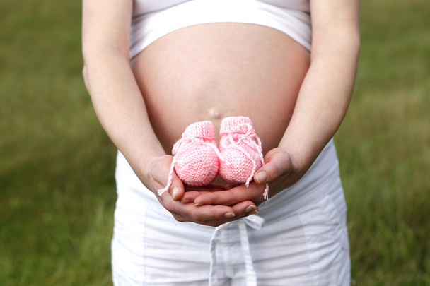 Pregnant woman outdoor with pink baby shoes in her hands - Photo, Image