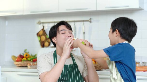 Ázsiai fiú szendvicset készített apának. A kisfiú szendvicset ad apának, és együtt eszik otthon a konyhában. A fiú szendvicset ad az apjának, boldog ázsiai családi koncepció. - Fotó, kép