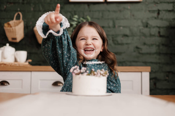 可愛い小さな子供の女の子はお祝いのドレスを身に着けている誕生日パーティーで装飾された花名ケーキから一口を取ります。. - 写真・画像