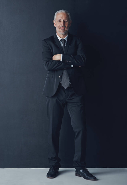 Studio portrait of mature businessman in suit, arms crossed and smile on dark background. Confidence, pride and professional career for happy executive man or senior business owner or successful ceo. - Photo, Image