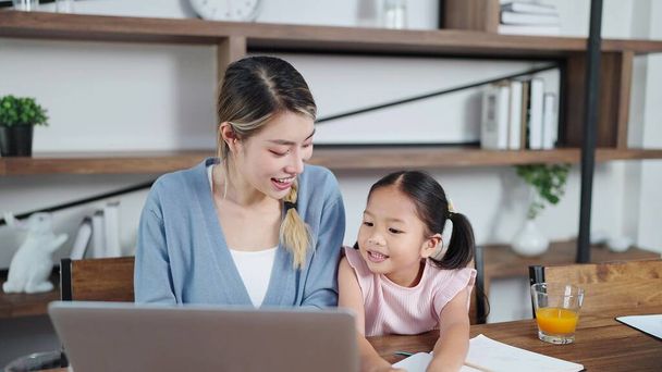 Szczęśliwa azjatycka matka i córeczka używają laptopa razem w domu. Oglądanie filmów lub przeglądanie Internetu. Samotna matka, matka i dziecko pojęcie relacji - Zdjęcie, obraz