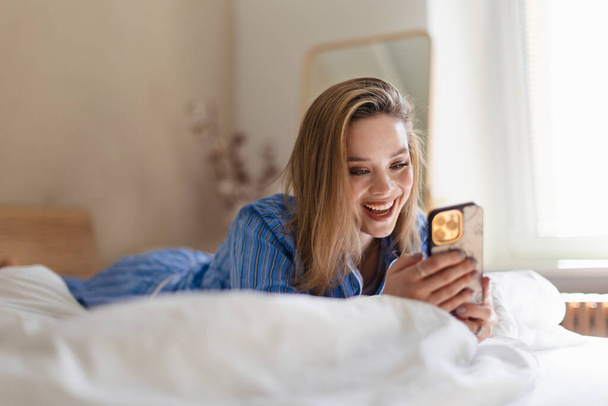 Young woman lying on her bed and scrolling a smartphone. - Φωτογραφία, εικόνα