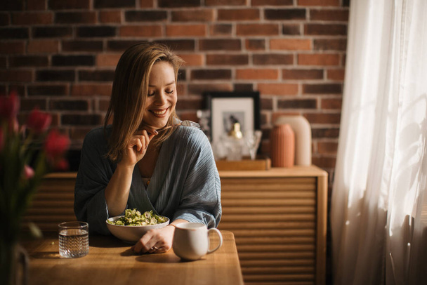 Young woman eating salad in the kitchen, concept of healthy eating. - Foto, imagen