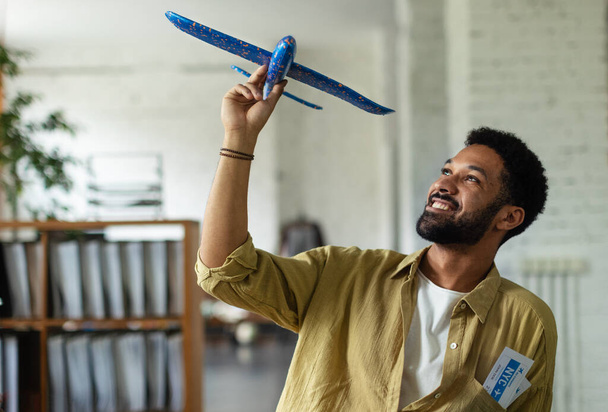 Giovane uomo felice che tiene il modello di aereo in un ufficio. - Foto, immagini
