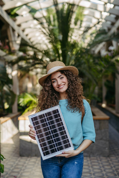 Young woman in a botanical garden holding solar panel, concept of green energy. - Foto, Imagen