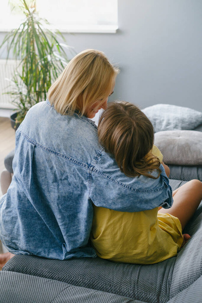 Young loving mother hugging her teenage daughter, mom demonstrating unconditional love for child, mommy cuddling supporting teen girl while spending time together at home. View from the back - Fotografie, Obrázek
