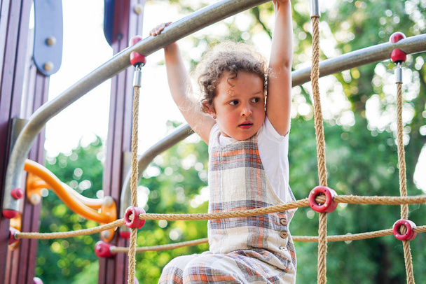 Pequena menina bonito com cabelo encaracolado brincando no parque infantil no parque público em um dia quente de verão, entretenimento e recreação para crianças - Foto, Imagem