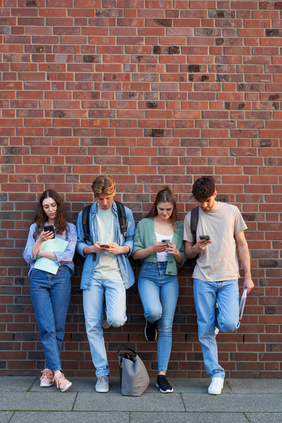 Groep universiteitsstudenten browsen telefoons naast universiteitscampus gebouw - Foto, afbeelding
