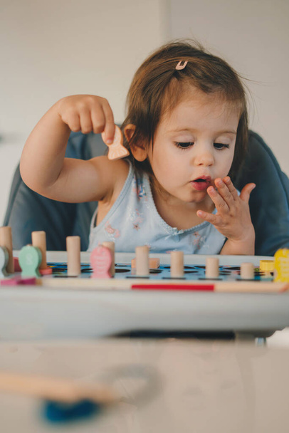 Gündelik giysiler içinde tatlı küçük bir kız masada oturuyor ve evde vakit geçirirken oyuncaklarla oynuyor. - Fotoğraf, Görsel