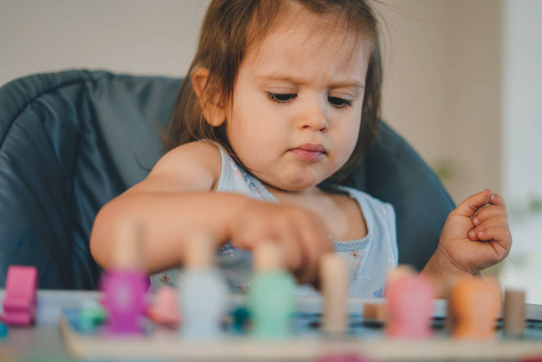 Милая маленькая девочка сидит за столом и играет с игрушками, проводя время дома - Фото, изображение