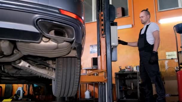 A car mechanic diagnoses the cars undercarriage. Raised car at repair station. Car service station - Imágenes, Vídeo