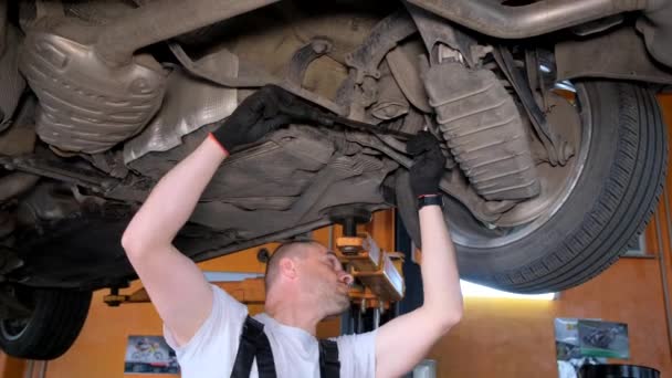 A car mechanic diagnoses the cars undercarriage. Raised car at repair station. Car service station - Záběry, video