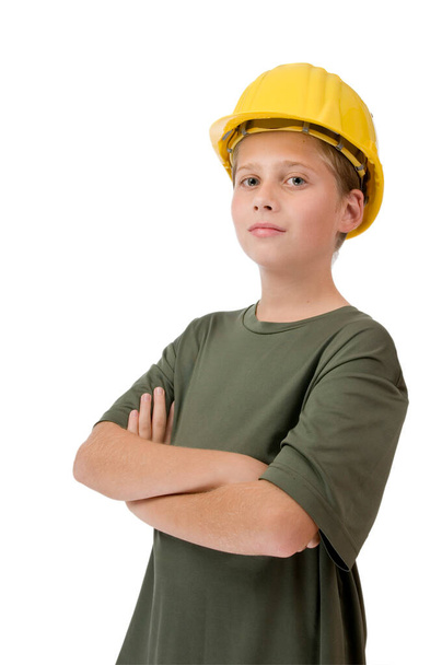 Three quarter torso view of a young Caucasian teenager wearing a yellow construction helmet, green t-shirt and crossed arms smiling proudly at the camera against white background - Foto, Imagen